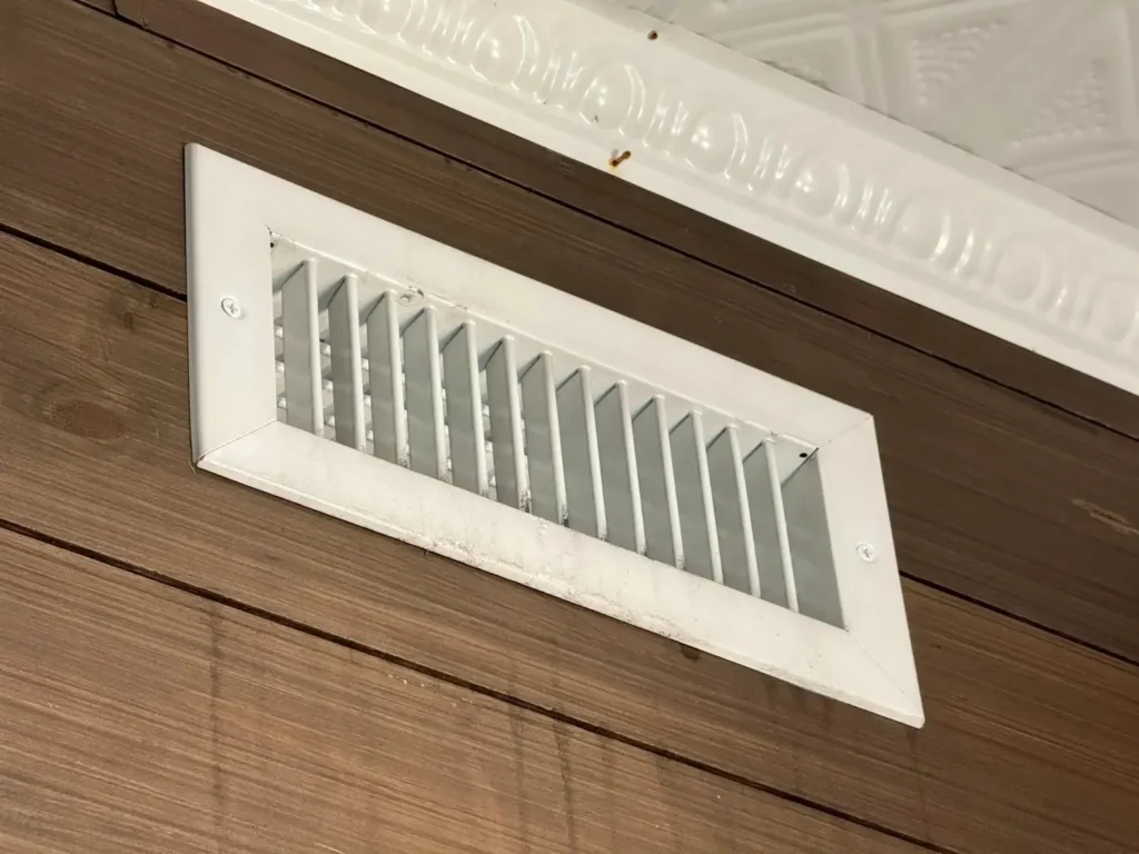 White rectangular HVAC air vent or register on a wooden wall.